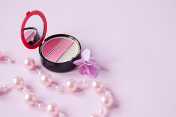 Lip gloss with mirror, flower and pearl necklace on pink background