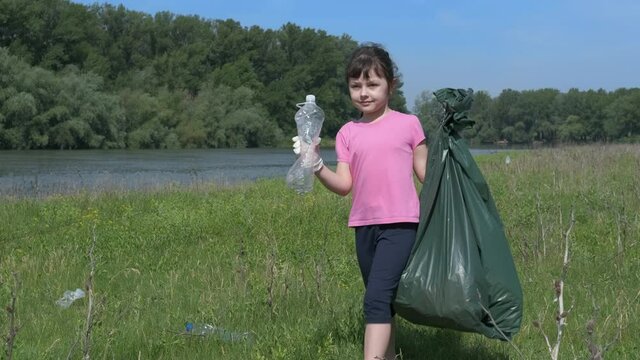 Plastic trash concept. Little girl collect plastic trash in nature. Child volunteer remove plastic from the river bank.