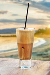 A greek cold coffee, freddo cappuccino placed on a wooden table over a beach background at sunset.