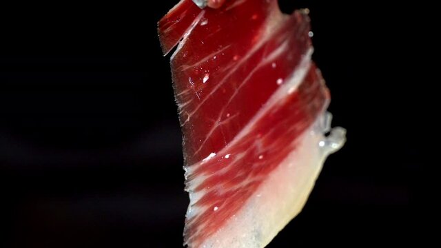 Superb image of a slice of Iberico ham, that moves with the wind and is shown to the camera in a short image detail. Very appetizing to eat that delicacy, with impressive red and white colors