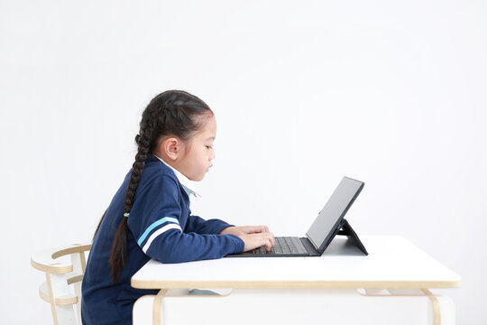 Asian Little Kid Girl In School Uniform Using Laptop On Table Isolated On White Background, Studio Shot