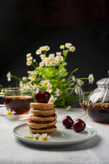 Homemade sweet mini pancakes with cherry jam and aromatic tea. Vertical orientation