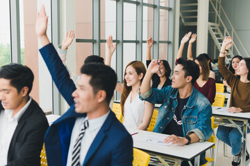 Asian male speaker is speaking at seminars and workshops to the people in the meeting. Those attending the meeting raised their hands to ask questions.