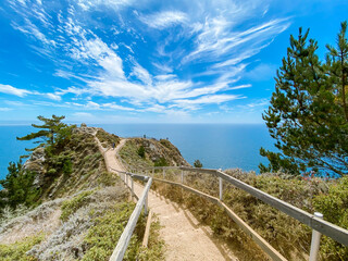 Fototapeta na wymiar Seascape. The walkway leads to the observation deck. Summer, sunny day. Blue sky with white clouds. Muir woods beach overlook, California, USA