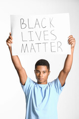 Sad African-American teenage boy with poster on light background. Stop racism