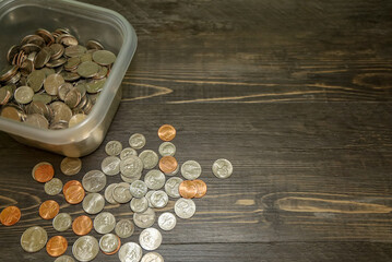 View of al container with a coins of multiple denominations and scattered pennies, dimes, nickels and quarters.