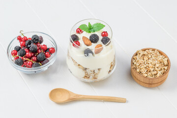A bowl of berries, a bowl of granola, and yogurt on a white table.