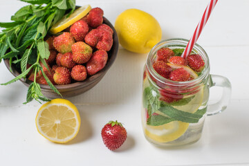 A bowl of strawberries and a large mug of cold water and lemon on a white table.