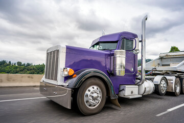 Fototapeta na wymiar Bright purple classic big rig semi truck with chrome accessories transporting cargo in tip semi trailer for carry heavy freights
