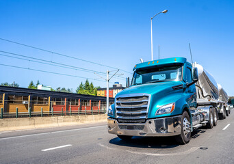Blue big rig day cab semi truck transporting load in two bulk semi trailers running on the road in...