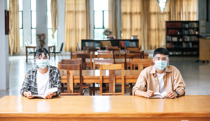 Men and women wearing masks sit and read in the library.