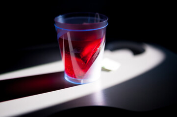 Glass of clear red tea on edge of table with light shining through it.