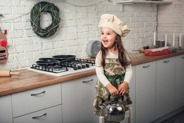 little girl in a chef's cap examines a kettle in the kitchen