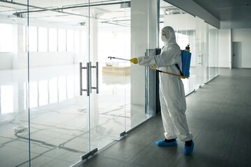 Sanitary worker sprays an empty business center with antiseptical liquid to prevent covid-19 spread. A man wearing disinfection suit cleaning up the shopping mall. Nobody, health, isolated concept. - obrazy, fototapety, plakaty