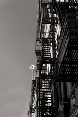 A black and white photo shows steam rising from a New York City Apartment building above a metal fire escape. 