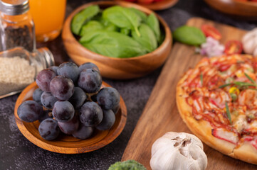 Black grapes on a wooden plate with tomatoes Orange juice and pizza.