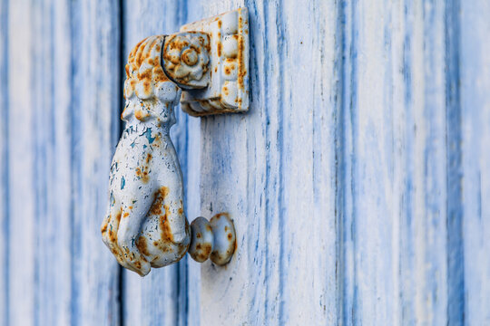 A rusted metal door knocker in the shape of a hand on a blue door in the town of Hautfort.