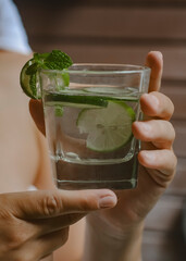 A glass with clean water, lime and mint in the hands of a girl in the bathroom