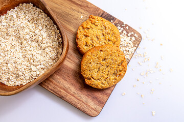 Homemade cookies with oatmeal on wooden board, with oat flakes container, over white background. 
