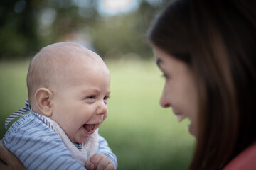 Bebé varón con su mamá en un parque haciendo muecas mirándose uno al otro