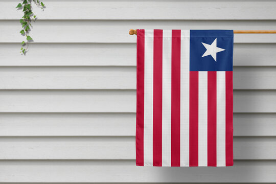 Liberia national small flag hangs from a picket fence along the wooden wall in a rural town. Independence day concept.