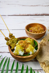 Sate padang is a traditional food satay beef from Padang Indonesia, completed with lontong, a traditional rice cake, and yellow special seasoning sauce on a wooden bowl, isolated on white table
