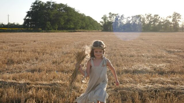 girl child in a dress runs through a mown wheat field at sunset