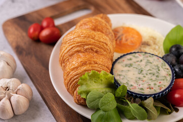 Breakfast consists of croissant, fried egg, salad dressing, black grapes, and tomatoes.