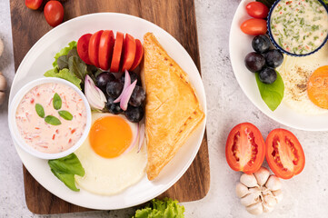Breakfast consists of bread, fried egg, salad dressing, black grapes, tomatoes, and sliced ​​onions.