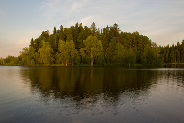 Fototapeta na wymiar The calm waters of the northern river in early summer. The river goes around a forested island