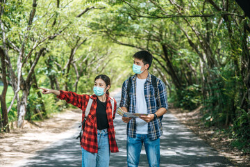 Male and female tourists wear medical masks and look at the map on the street.