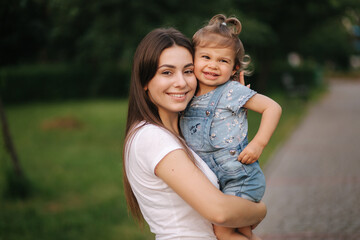 Fototapeta na wymiar Portrait of beautiful mom with adorable little girl. Happy family outdoors. Daughter hug mum