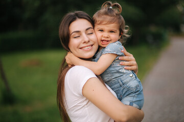 Fototapeta premium Portrait of beautiful mom with adorable little girl. Happy family outdoors. Daughter hug mum