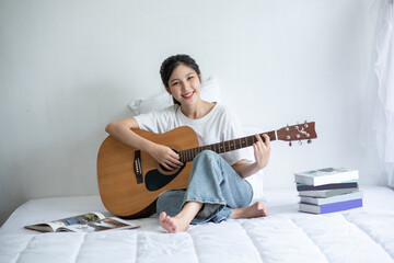The girl sat and played the guitar on the bed.