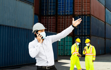 Manager Engineers with hard hat assign by smart phone with team for working and architects and engineers at the containers box in warehouse background.Business logistics site.