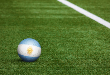 Argentina flag on ball at soccer field background. National football theme on green grass. Sports competition concept.