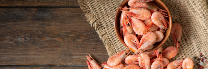 Shrimp in a wooden bowl on a brown wooden table. Lots of shrimp in a bowl and on the table. Shrimp close-up. Rustic style. Banner	