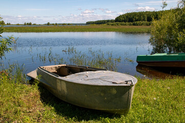 Boats stand, leaning out of the water onto the riverbank overgrown with green grass.
