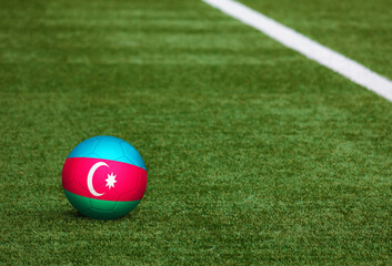 Azerbaijan flag on ball at soccer field background. National football theme on green grass. Sports competition concept.