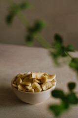Pretty small bowl with sliced banana on table in the kitchen with mint leaves decoration. Tasty and healthy vegetarian food 