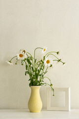 A bouquet of daisies in a vase on the table. Rural vintage still life. Vertical composition for the design of the cards. White table and white concrete background with space for text.