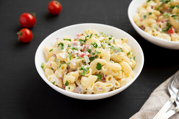 Homemade Macaroni Salad in a white bowl on a black background, side view.