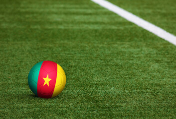 Cameroon flag on ball at soccer field background. National football theme on green grass. Sports competition concept.