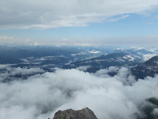 View onto Austrian valley from mountain top through white clouds 