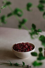 Pretty small bowl with bright red dried cranberries in the kitchen with mint leaves decoration. Tasty and healthy vegetarian food 