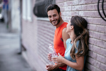 Fototapeta premium Athletic couple is having a rest after jogging in the city. Happy couple enjoying in the morning. 