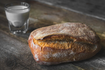 loaf of bread and glass with milk on wooden table