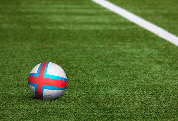 Fototapeta na wymiar Faroe Islands flag on ball at soccer field background. National football theme on green grass. Sports competition concept.