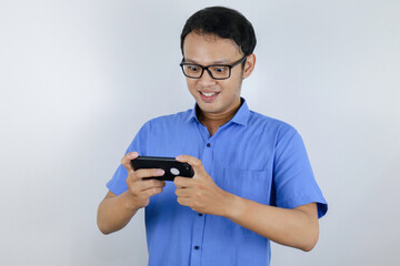 Asian young man enjoy and smile on the smartphone when play game. Indonesian man wearing blue shirt.