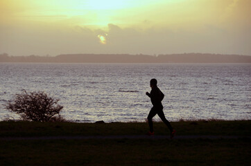 Silhouette of a person jogging in evening light, with the sea as background.